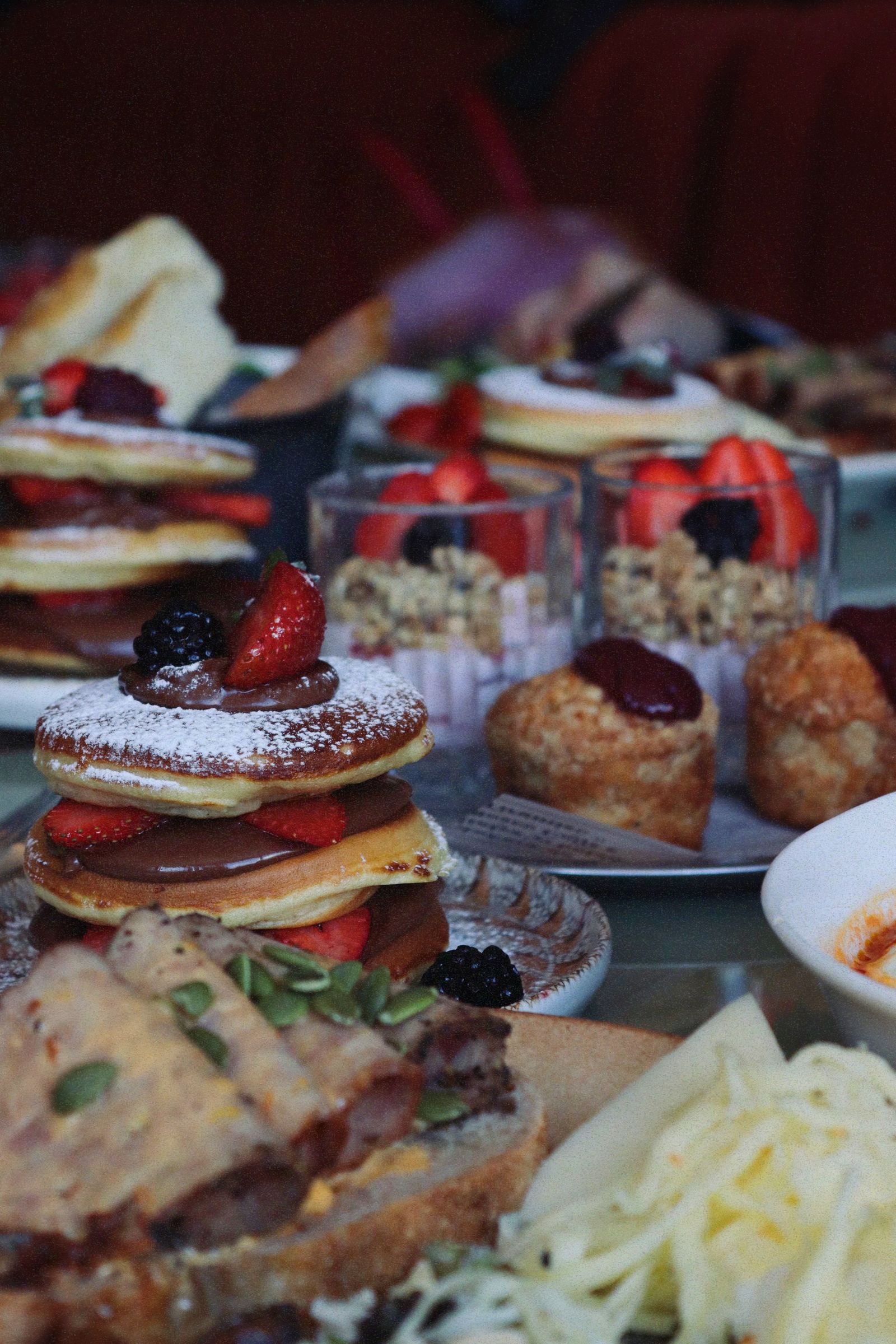 A generous café breakfast table with pancakes, pastries, berries and juice